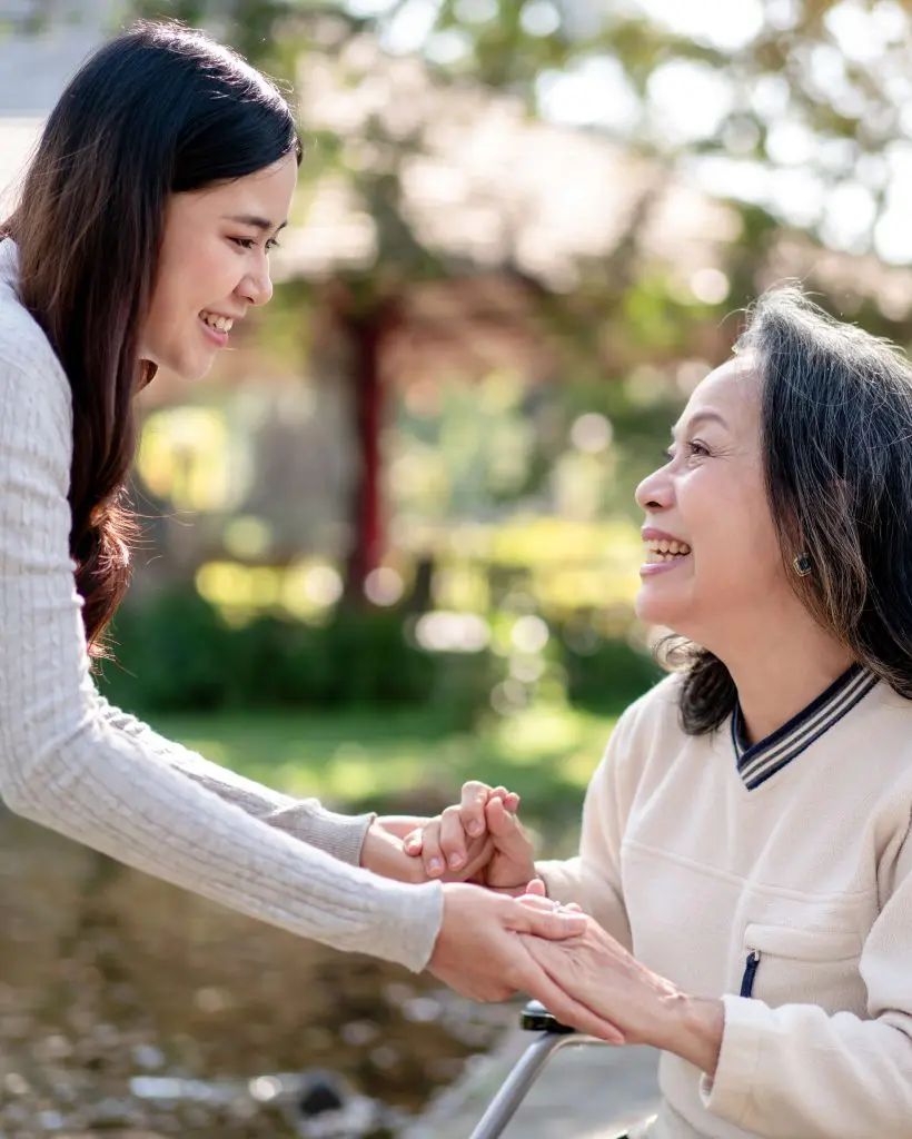 Elderly grandmother in wheelchair with daughter smiling enjoying at the garden in the morning