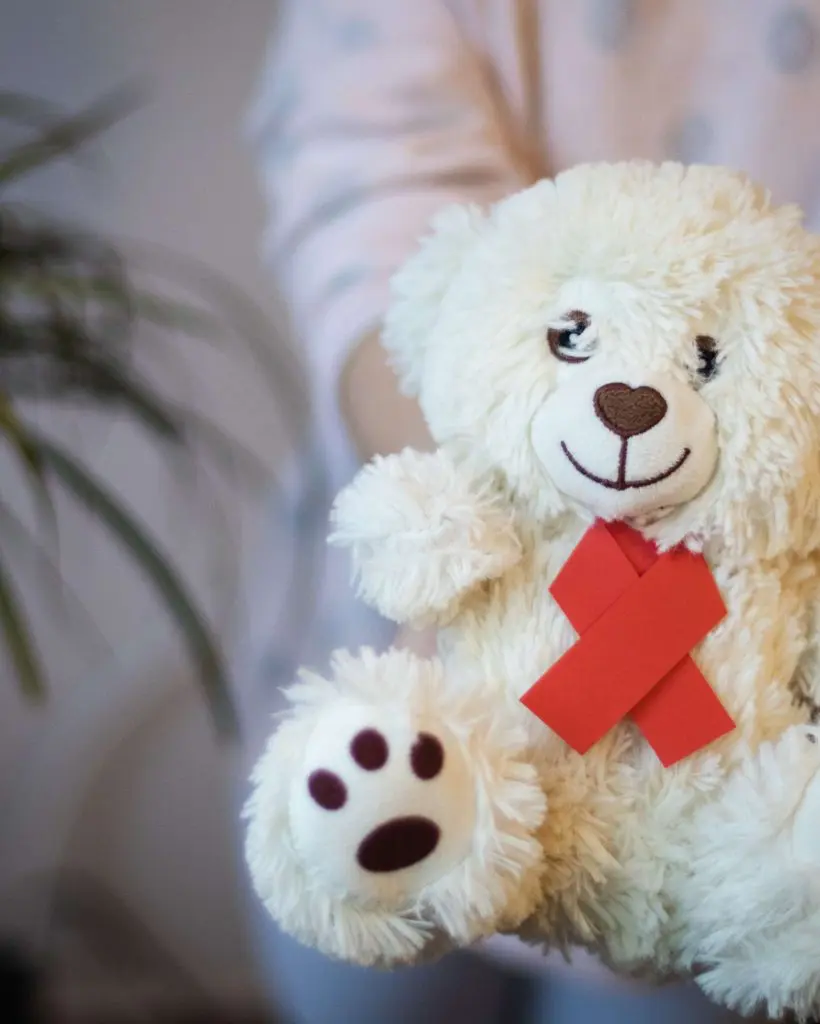 The girl holds in her hands a toy bear with a red ribbon.